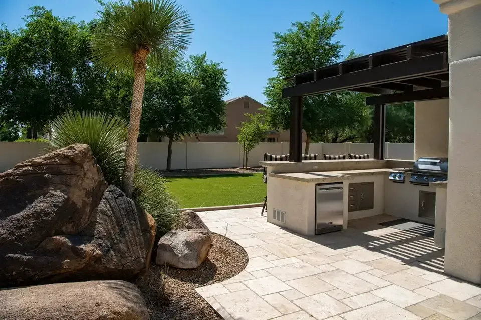 Outdoor kitchen under a pergola with paver patio and boulders